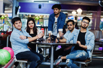 Group of five south asian peoples having rest and fun at bowling club, sitting on table and drinking soda drinks at glass bottles.
