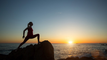 Silhouette of young woman doing fitness exercises on the beach at sunset.