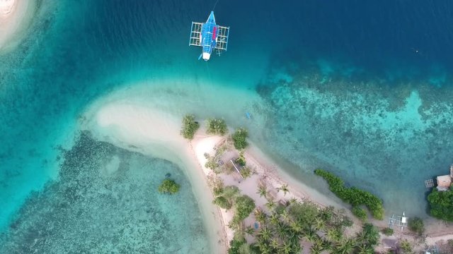 Drone image of a bungalow village, with a traditional boat in the front of the island. Somewhere in Palawan, Philippines