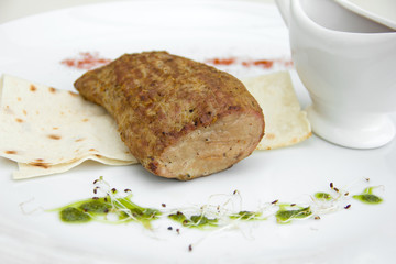 grilled meat on a white plate, sauceboat with sauce, restaurant serving