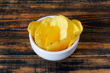 Golden potato chips on wooden background.
