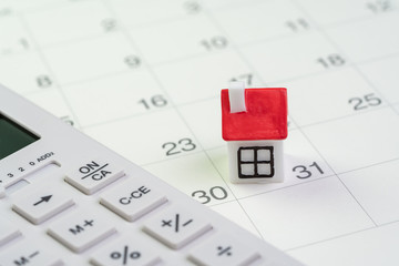 House mortgage payment and installment schedule concept, small miniature house on end of month calendar with calculator
