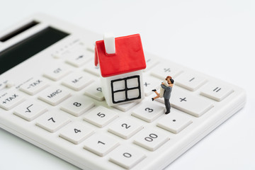 Family goals, building future with house cost calculation, mortgage and home loan or real estate concept, miniature couple figure with small house on white clean calculator on white background