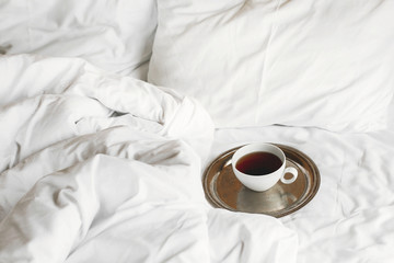 Happy morning.Tea in white cup on metal vintage tray on white bed. Enjoying morning concept, coffee in bed. Bed with white sheets in hotel room or home bedroom with hot drink. Space for text