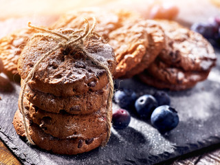 Serving food on slate onto wooden table. Oatmeal cookies biscuit with blueberry on picnic dark tiles countrylike. Chocolate chip cookies tied with string sun flare.