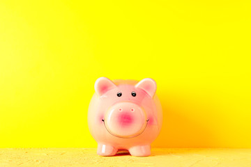 Happy piggy bank on yellow table against color background, space for text. Finance, saving money