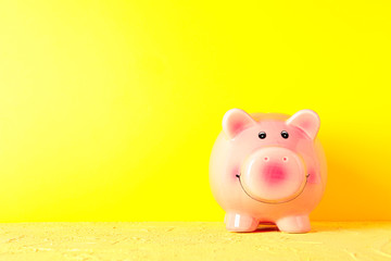 Happy piggy bank on yellow table against color background, space for text. Finance, saving money