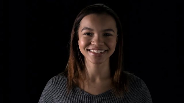 Lockdown Of Beautiful Teenage African Girl With Straight Hair Standing Against Black Wall, Looking At Camera With Smile On Her Face