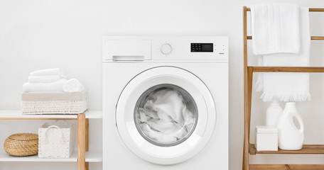 Washing machine with laundry and shelves on white wall background