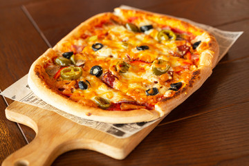 Pizza with jalapeno chillies and olives on wooden pizza board, selective focus.