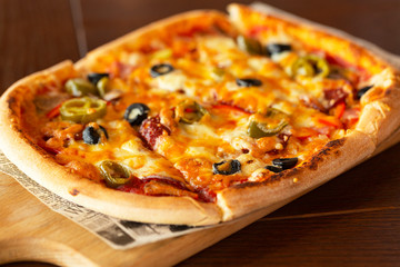 Pizza with jalapeno chillies and olives on wooden pizza board, selective focus.