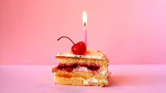 Cupcake with cherry and burning candle for the birthday on pink background