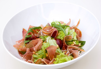 salad with vegetables, greens and prosciutto, white plate, restaurant serve