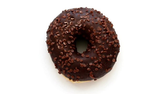 Chocolate donut turns around on white background, top view