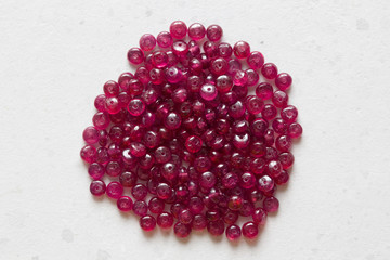 Ruby stones lie on a white table, a white background. Natural stones ruby, ruby beads. Pink ruby...