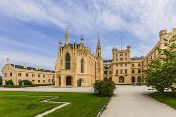 Fototapeta na wymiar Lednice, Czech Republic - May 28 2019: Famous Lednice castle in South Moravia with yellow facade. Green lawn, trees and sand footpath in foreground. Sunny spring day, blue sky, white clouds.