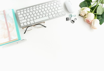 Flat lay women's office desk. Female workspace with laptop,  flowers pink roses,  accessories, notebooks, glasses,  on white background. Top view feminine background.Copy space. 