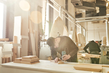 Worker grinds the wood of angular grinding machine at his workstation