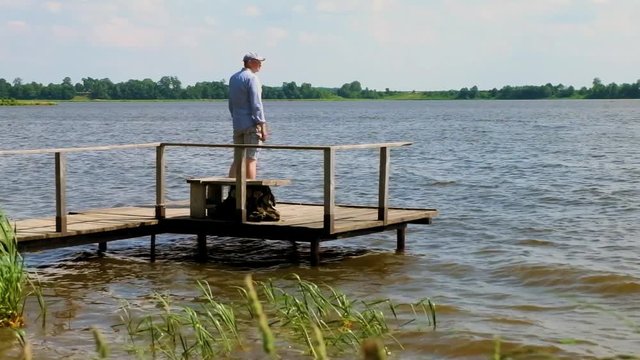 man walks and stands on  pier at the lake in windy weather