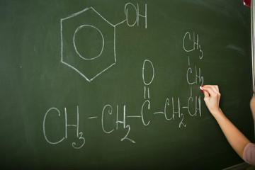 the hand of a chemistry teacher is writing on the blackboard. the teacher writes on the blackboard chemical formula. the formula of the hydrocarbon. hand writing with chalk