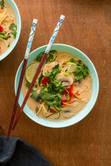 thai curry chicken ramen in blue bowl on wooden background, top view