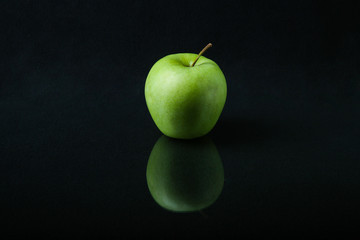 green apple on a black background with reflection