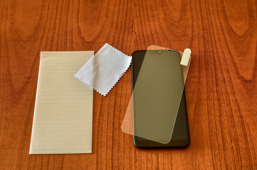 On the wooden table rest the smartphone, the panel and the protective glass to be installed