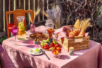 summer table with rose tablecloth with two colourful glasses and lemonade wattled basket with bread croissant and wheat outside sun rays bokeh lights