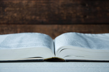 A large book lies open on a wooden table.