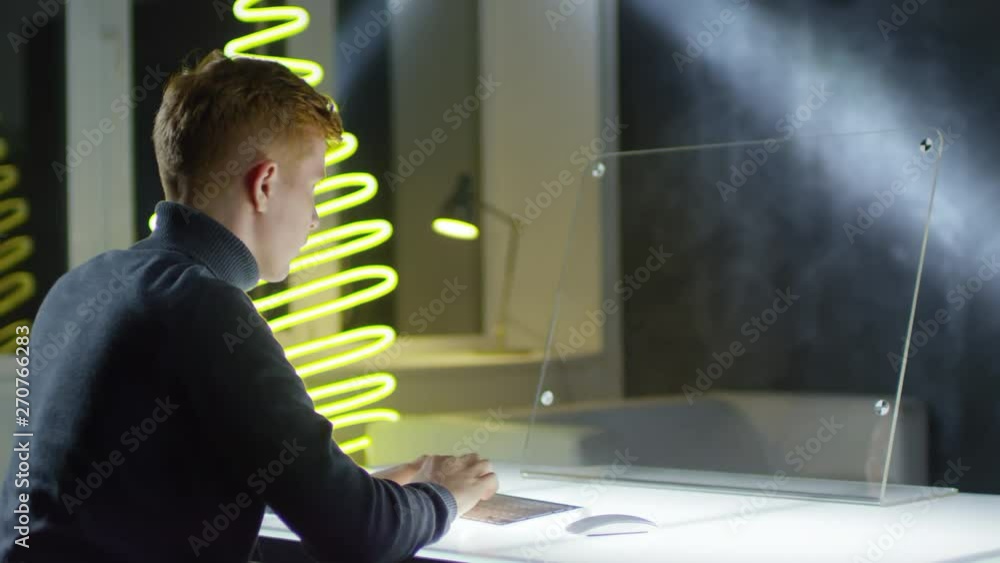 Aufkleber back view of young caucasian man sitting at see-through ar screen of futuristic pc and typing on wir