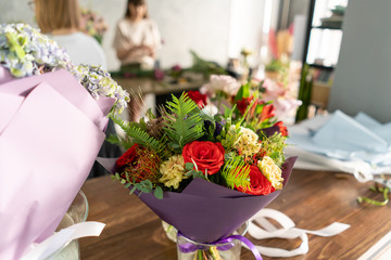 In the foreground a bouquet in a vase on the background of a flower shop. People work, Profession florist. Summer bouquet. Flowers delivery