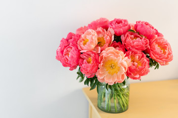 Coral peonies in a glass vase on wooden table.. Beautiful peony flower for catalog or online store. Floral shop concept . Beautiful fresh cut bouquet. Flowers delivery. Copy space