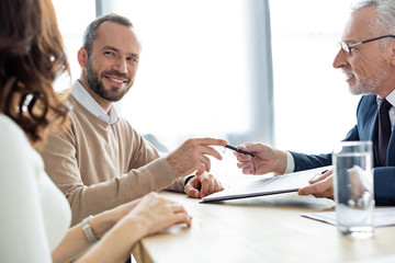 selective focus of car dealer giving pen to happy man looking at woman in office