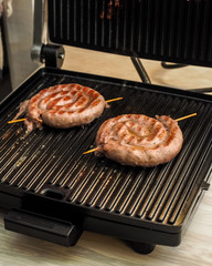 Fried spiral sausages on an electric barbecue BBQ grill. Homemade menu.