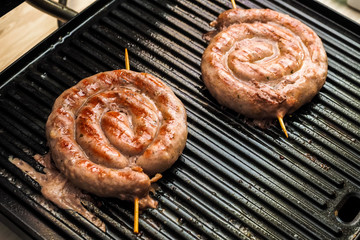 Fried spiral sausages on an electric barbecue BBQ grill. Homemade menu.