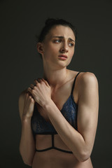Half-length portrait of young sad woman in underwear on dark studio background. Sadness, depression and addiction. Concept of human emotions, feminism, woman's problems and rights, mental health.