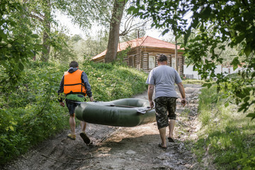 Adult man and a teenager together carry a rubber boat