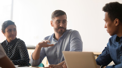 Diverse colleagues talk discussing ideas during meeting in office