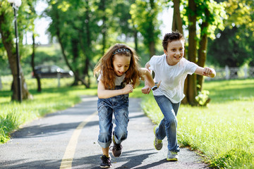 Fototapeta premium Brother and sister running in the summer park on sunset. Cheerful children. Little girl and boy are doing sports outdoors, best friends. Childhood concept
