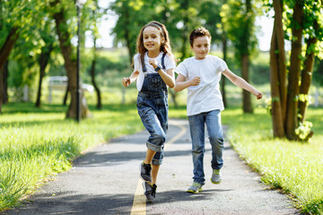 Obraz premium Brother and sister running in the summer park on sunset. Cheerful children. Little girl and boy are doing sports outdoors, best friends. Childhood concept