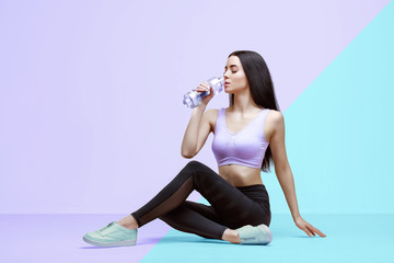 Amazing woman in trendy sportswear drinking water from bottle to stay hydrated after workout....