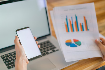 Business woman hand with Financial charts and mobile phone over laptop on the table .