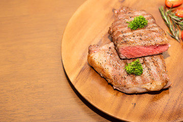 Fototapeta na wymiar Fresh cooked half cut beef sirloin with cherry tomato and rosemary on top with parsley, Wood background, Copy space on the left