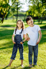 Cheerful little girl and boy hugs and playing on green grass. Brother and sister in wet clothes in the summer park. Best friends. Childhood concept.