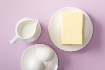 top view of butter, milk jug and boiled eggs on white plates on violet background
