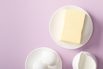 top view of butter, milk and boiled eggs on white plates on violet background