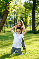 Cheerful little girl and boy fights on green grass and smiling. Brother and sister in wet clothes in the summer park. Best friends. Childhood concept.