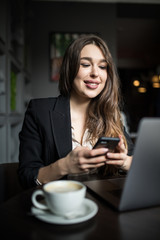 Smiling woman in cafe using mobile phone and texting in social networks.