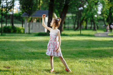 Cute little girl on the meadow in rose dress on sunset. Posing like ballerine. Childhood concept.