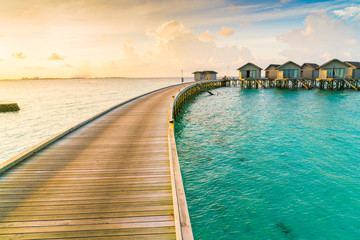 Beautiful water villas in tropical Maldives island at the sunrise time .